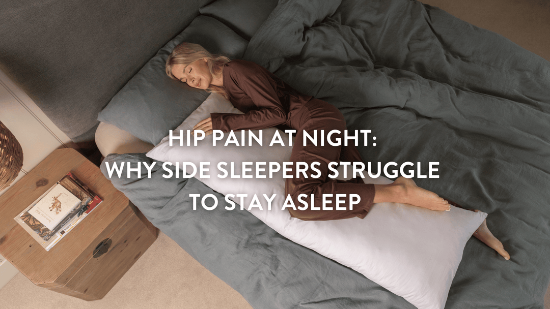 Person sleeping on their side in a large double bed with grey linen using a Putnams Sports Recovery Pillow to relieve hip pain at night